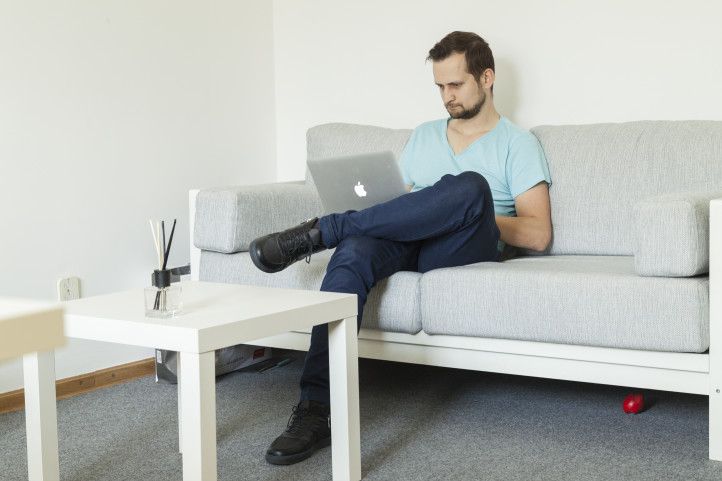 Maciej Woźniak siedzi na kanapie i pracuje na laptopie